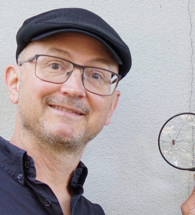 Mies suurennuslasi kädessään hymyilee kameralle