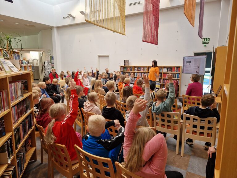 Lapsia kuuntelemassa tietokirjailijan vierailua innokkaasti viitaten.