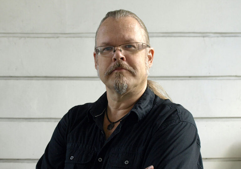 Mies mustassa kauluspaidassa katsoo kameraan